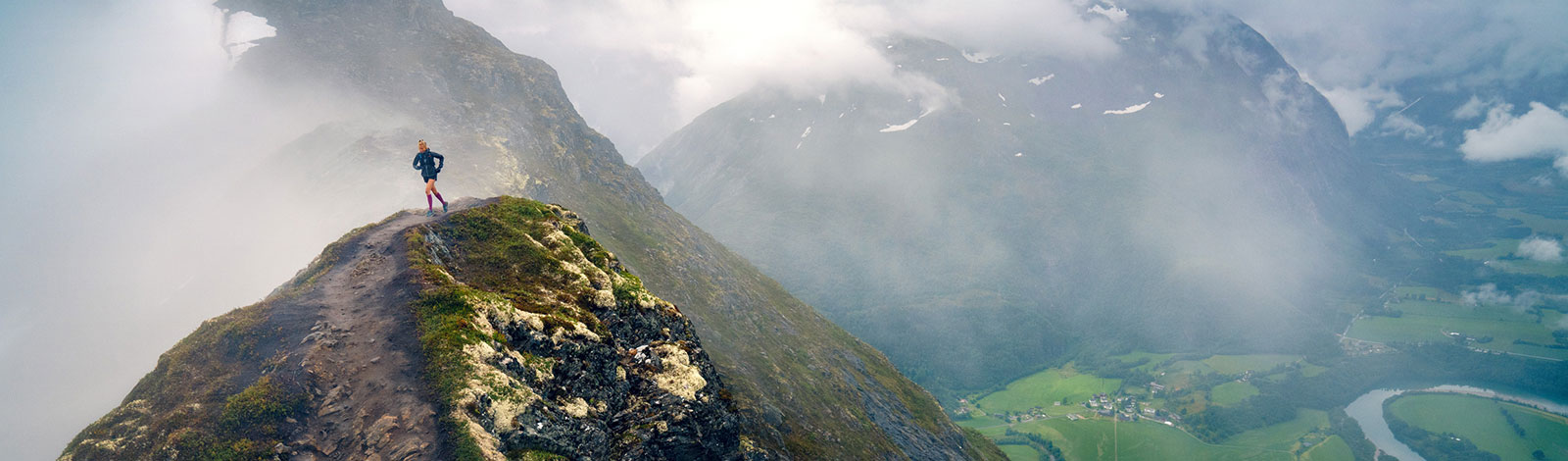 Il paesaggio di montagna magro a sinistra significa che una donna corre su uno stretto sentiero di montagna vicino alla cima a destra, la valle può essere vista con un piccolo posto e un fiume