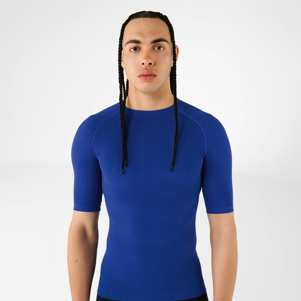 Un uomo indossa una maglia a compressione blu e guarda con sicurezza verso la fotocamera.