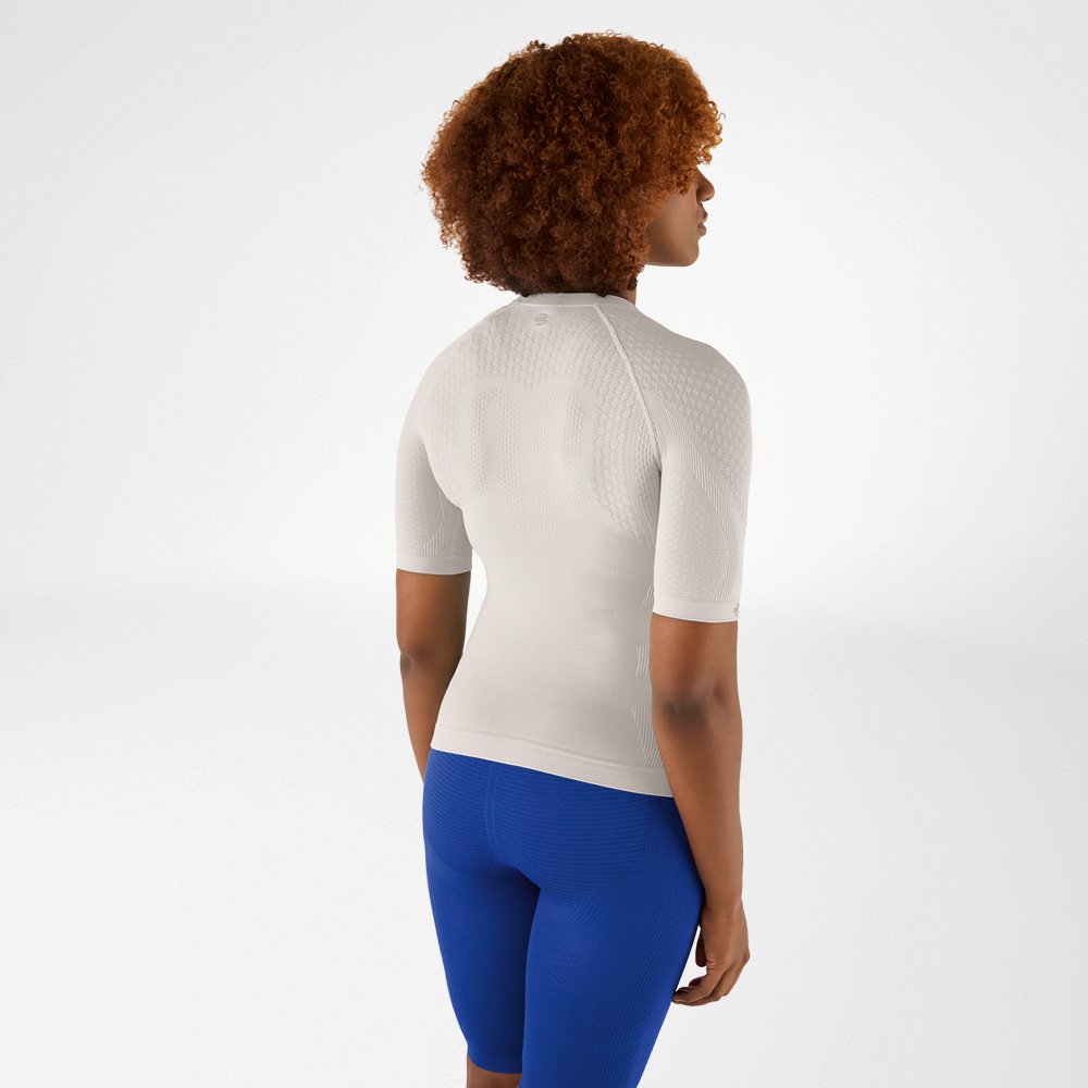 Vista posteriore di una donna con capelli ricci in una maglia a compressione grigio argento e leggings blu, che guarda leggermente di lato.