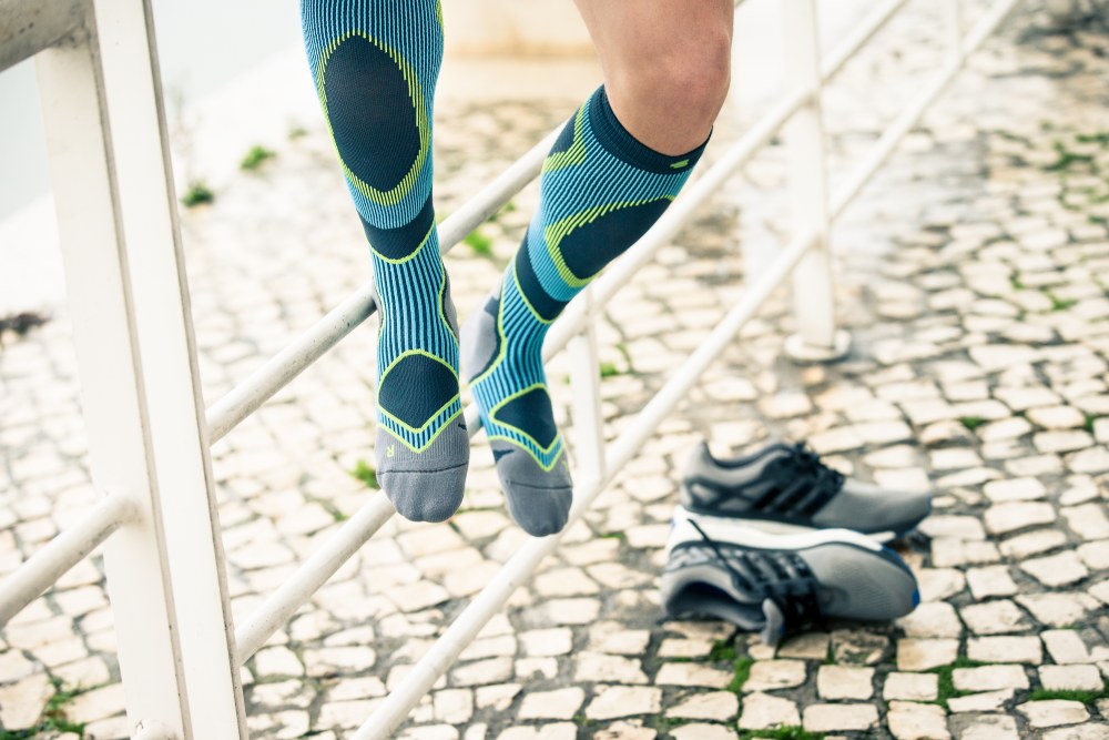 L'uomo con i calzini da corsa blu e grigio si siede su una recinzione e si è tolto le scarpe