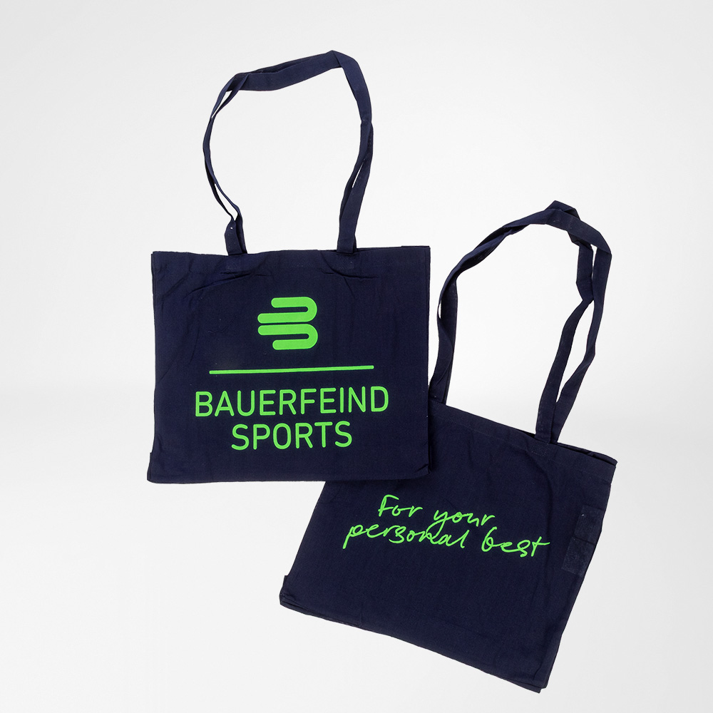 Porta con te la motivazione – con stile e carattere. Due borse in cotone blu scuro di Bauerfeind Sports con stampa verde fluo. Una mostra il logo Bauerfeind Sports, l’altra lo slogan "For your personal best".