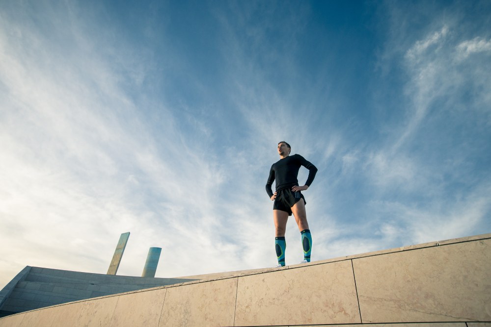 Il corridore con abiti da corsa neri e calzini in corsa blu è determinato sul muro di un edificio moderno e guarda a distanza