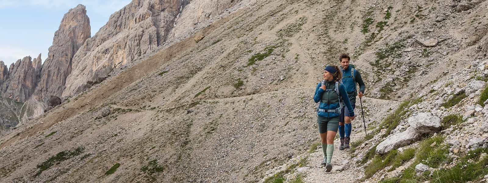 L'uomo e la donna camminano giù da una montagna con bastoncini escursionistici e portano calzini da trekking