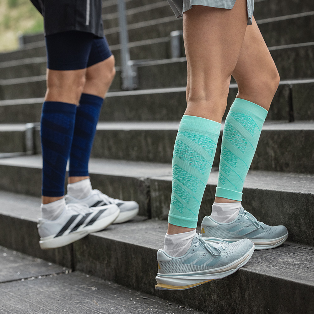 Due runner durante un allenamento sulle scale all’aperto. Indossano Run Performance Sleeves con compressione in mint e blu navy per stabilizzare i polpacci e stimolare la circolazione.