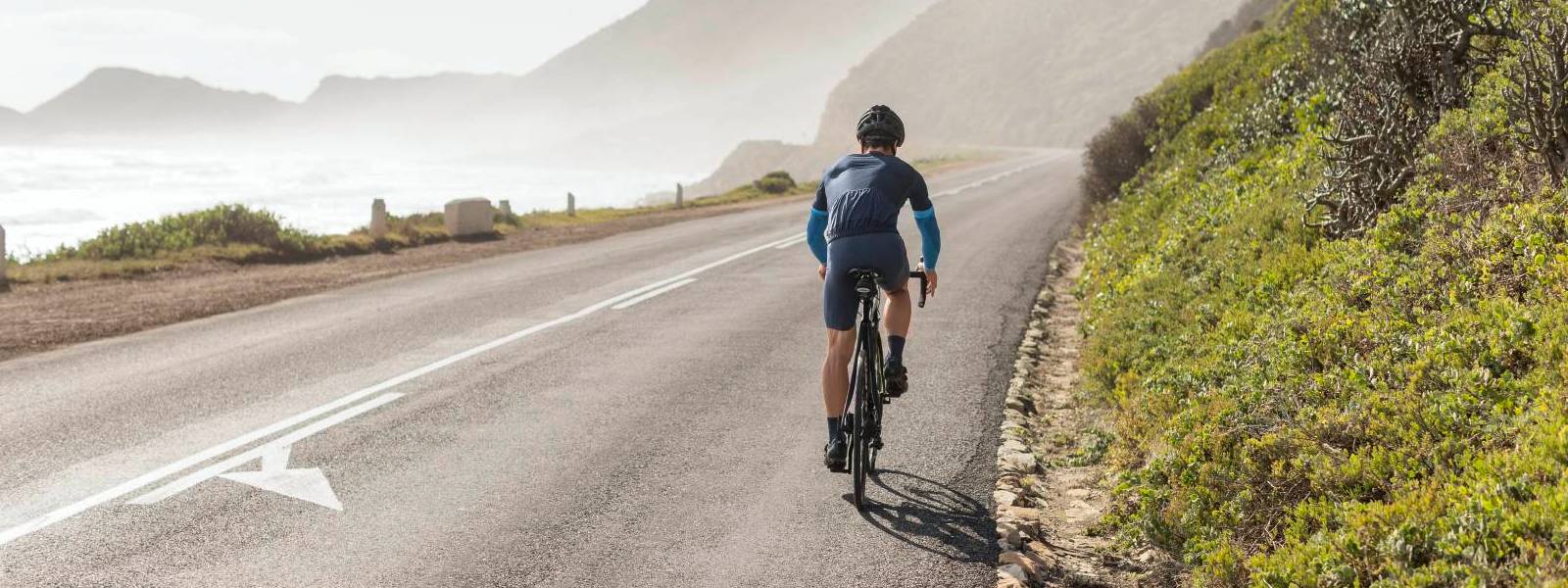 Bike di guida maniche a braccio I ciclisti indossano maniche a braccio blu e guida su una strada sul pendio con una vista sul mare