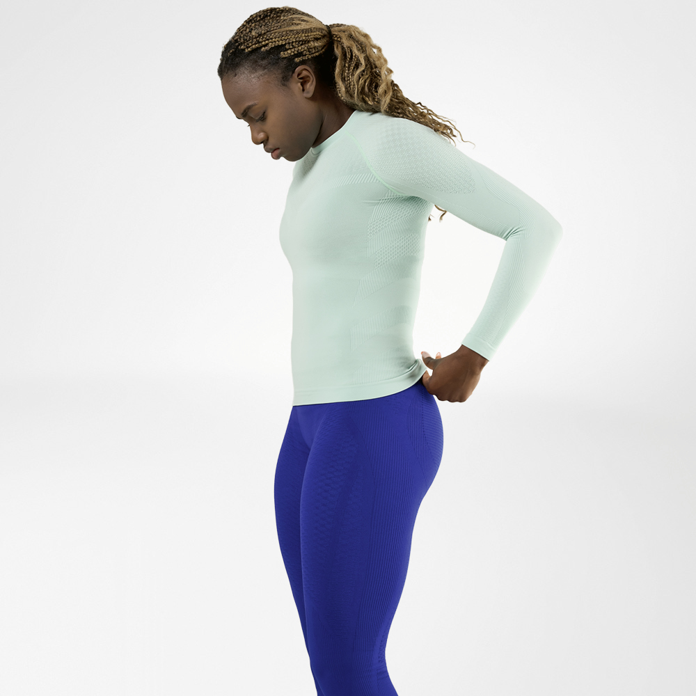 Donna con maglia a maniche lunghe verde menta e pantaloni a compressione blu, vista laterale