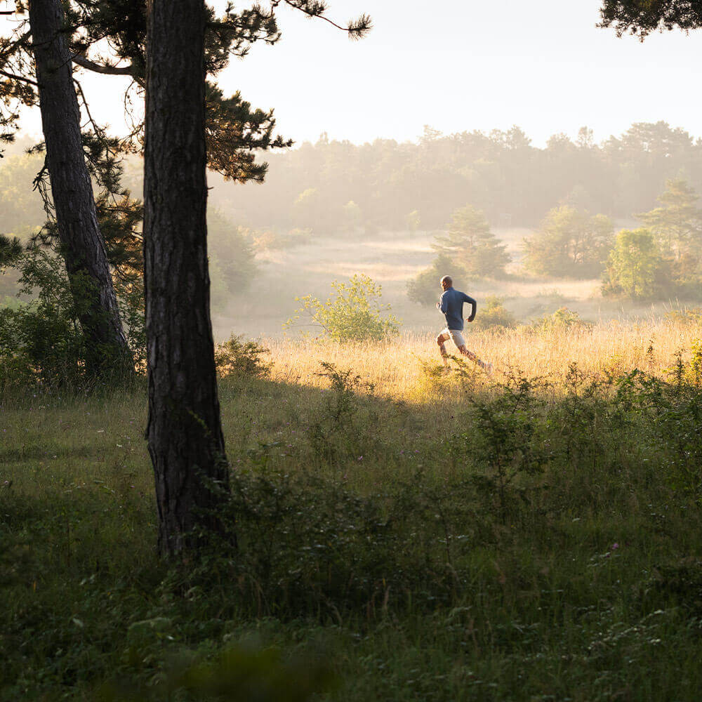 Sport in azione L'uomo corre sopra un prato in primo piano un albero sullo sfondo sono le colline