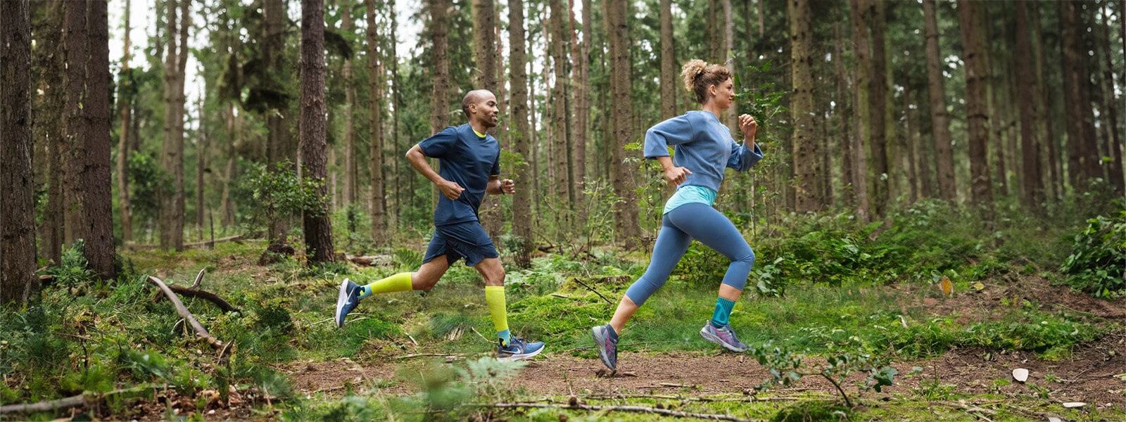 Una donna e un uomo corrono attraverso un fitto bosco e indossano bende