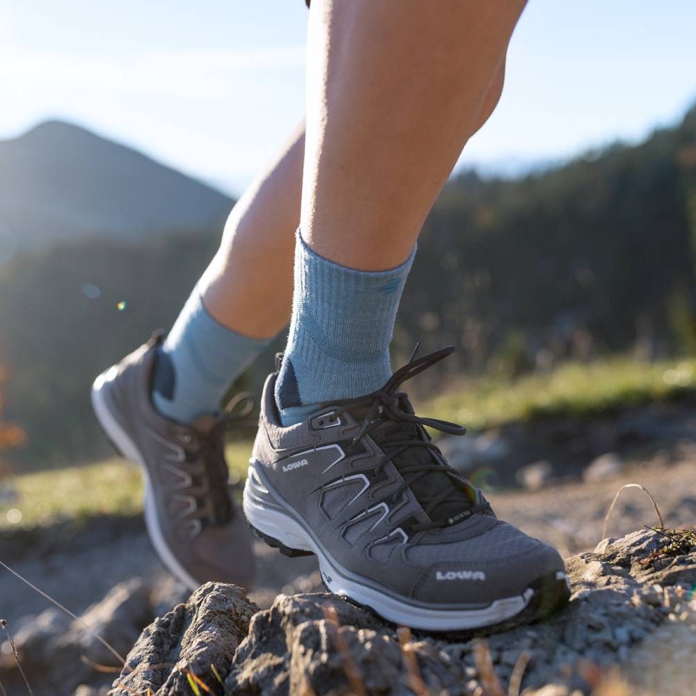 Nahaufnahme eines Wanderers, der Merino Outdoor Socks in Granatfarbe trägt und einen felsigen Pfad hinaufsteigt. Die Socken sind in Wanderschuhen getragen und reichen bis zur Wade.