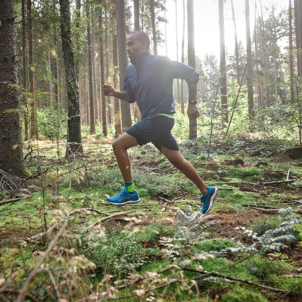 Un uomo corre attraverso un fitto bosco e indossa una fasciatura per l'Achille. 