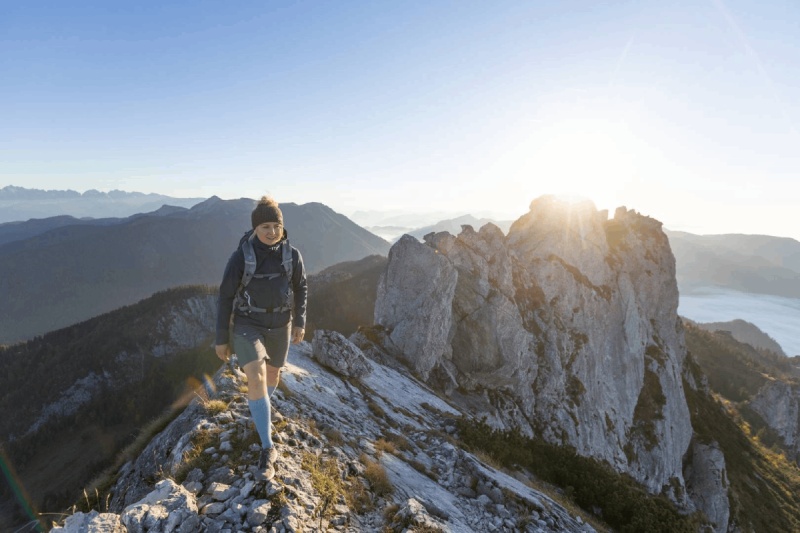 Escursioni in leggerezza - Outdoor Merino Compression Socks per sentieri impegnativi! Un'escursionista con Outdoor Merino Compression Socks cammina su un sentiero di montagna all'alba. Questi calzini a compressione offrono supporto ottimale e comfort per escursioni impegnative.
