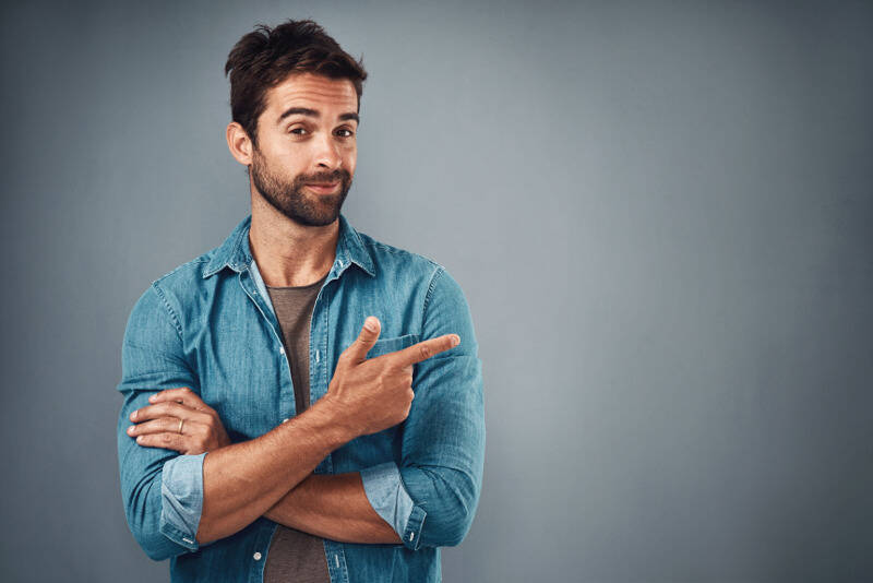 L'uomo sorridente in una camicia di jeans si mostra con il dito indice sul lato