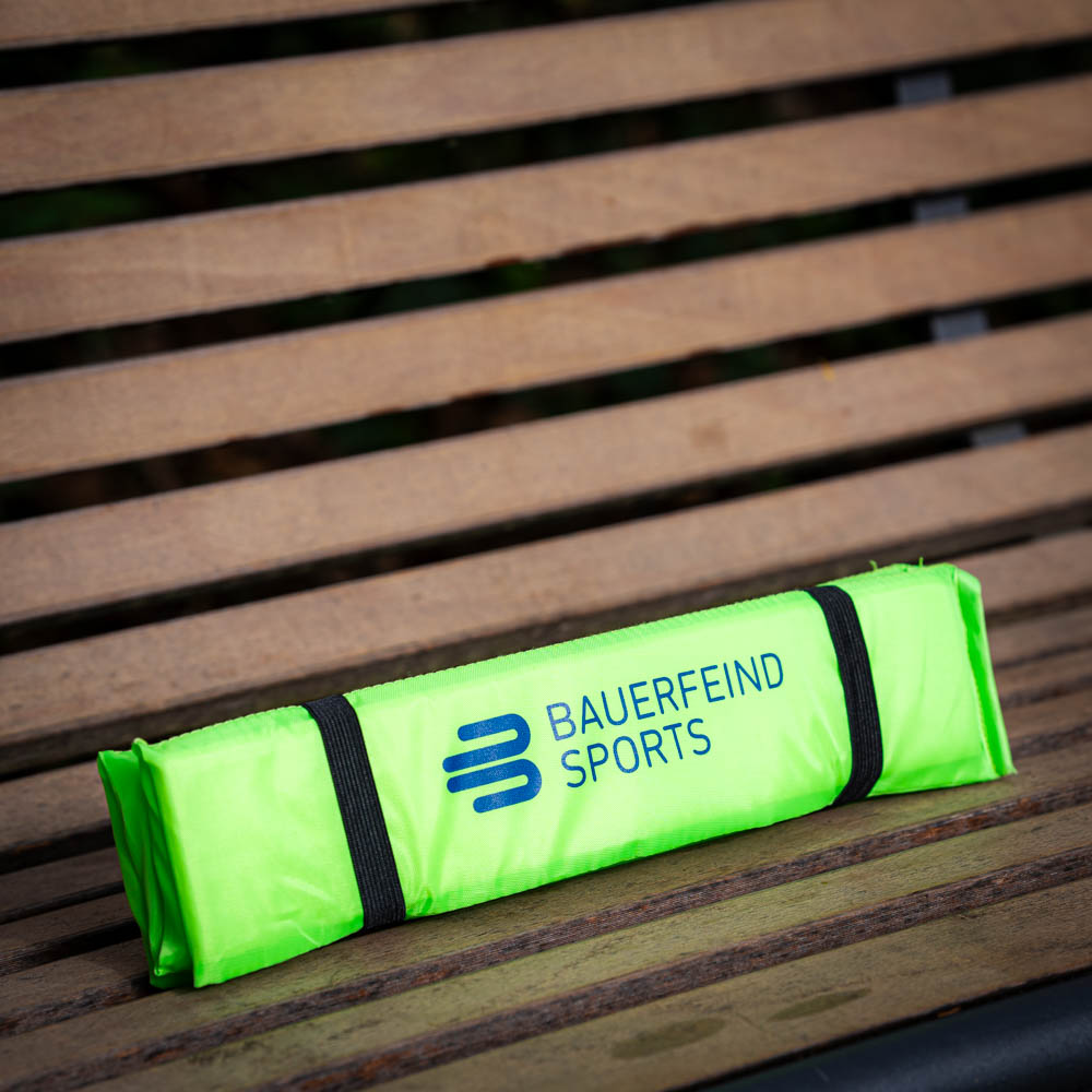 Pratico cuscino da seduta per spostamenti Cuscino da seduta Bauerfeind Sports piegato in verde brillante, riposto in sicurezza su una panca di legno.