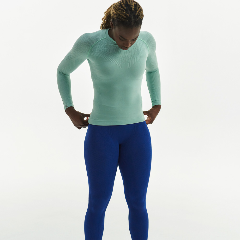 Il nuovo set di indumenti compressivi per donne Donna con top a compressione verde menta e pantaloni a compressione blu scuro guarda il pavimento e tiene le mani sui fianchi