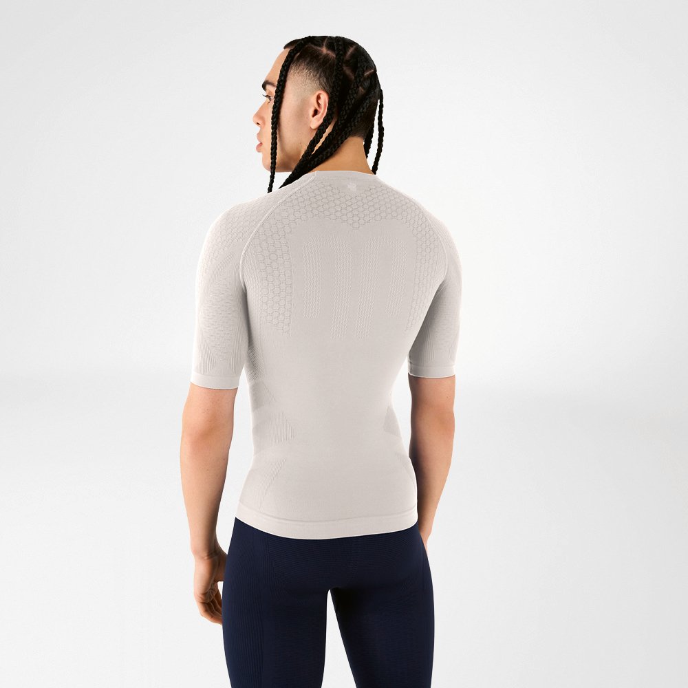 Un uomo indossa una maglia a compressione grigio argento, di spalle alla fotocamera, guarda oltre la spalla.