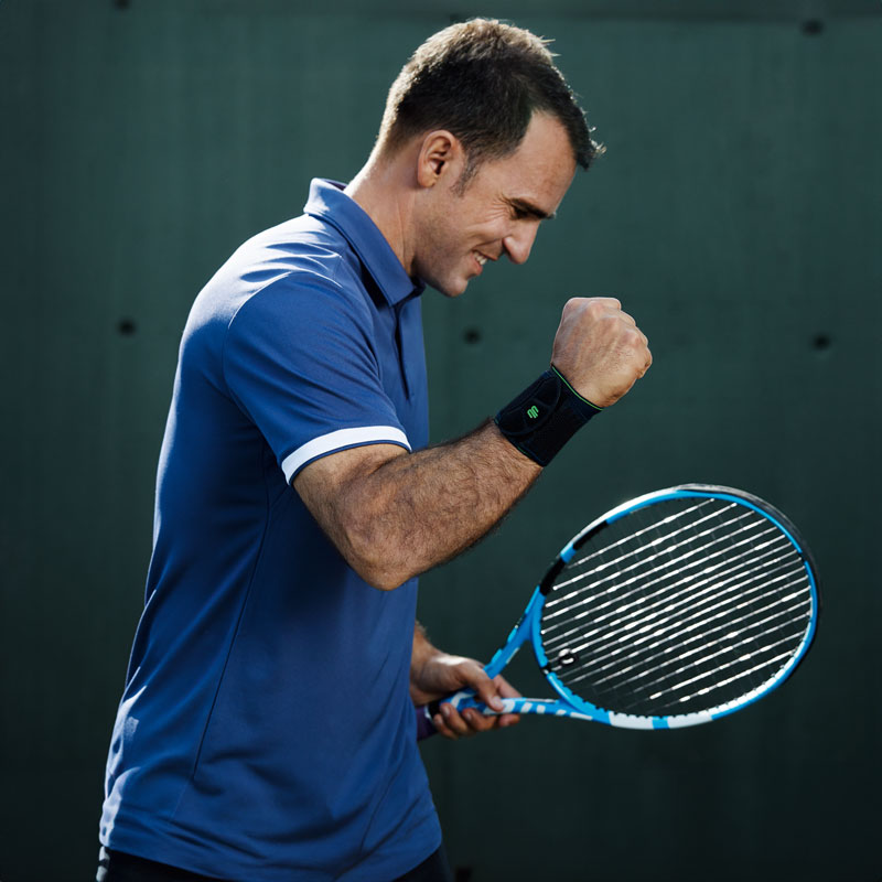 Tennis Player con una benda del polso nero solleva il braccio libero e si aggrappa il pugno soddisfatto