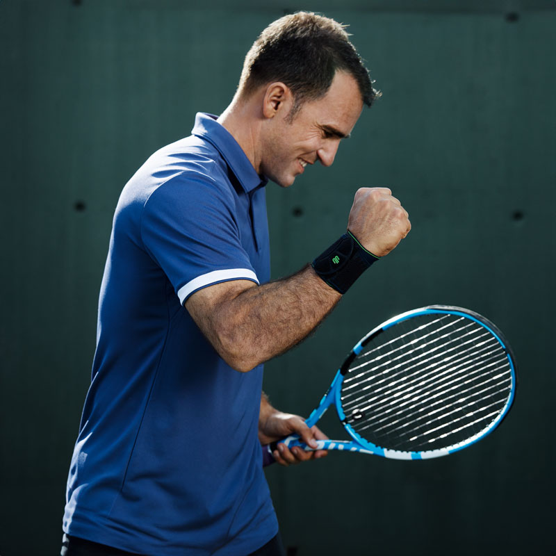 Più stabilità e precisione nel tennis con supporto al polso sportivo Tennis Player con una benda del polso nero solleva il braccio libero e si aggrappa il pugno soddisfatto
