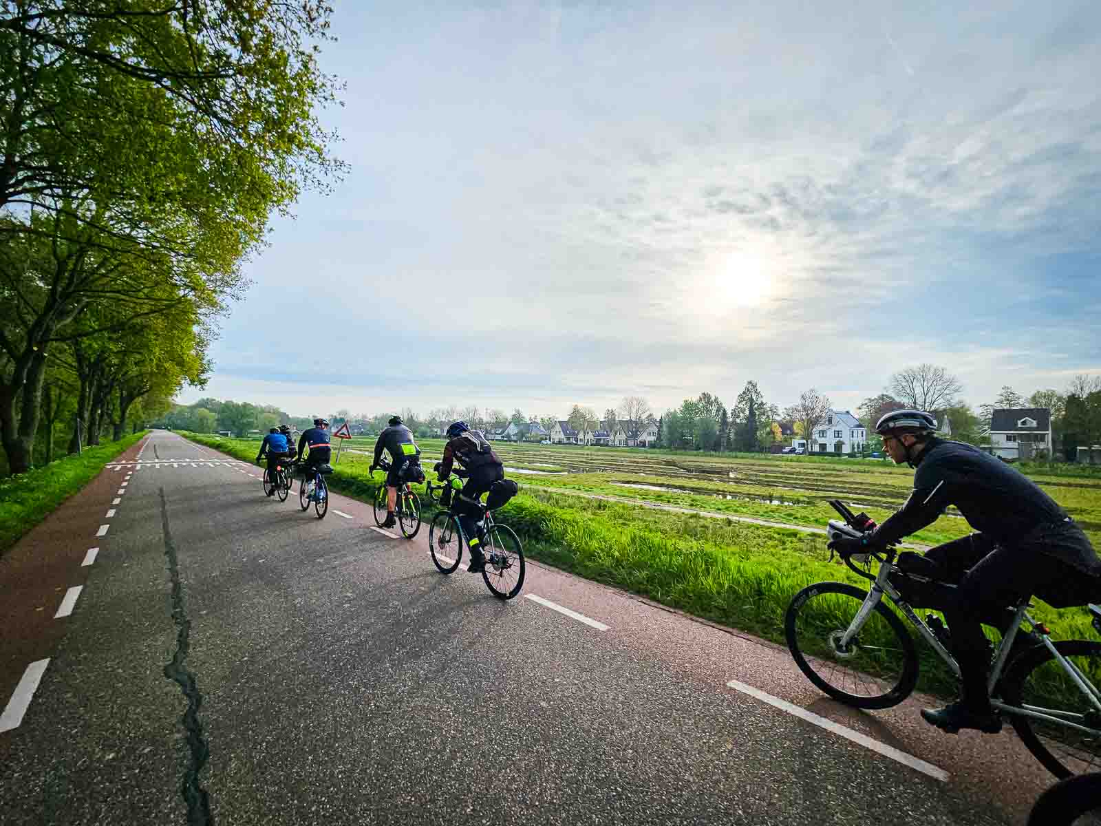Fila di ciclisti alla Corsa intorno ai Paesi Bassi Diversi ciclisti pedalano l'uno dietro l'altro su una strada della Corsa intorno ai Paesi Bassi