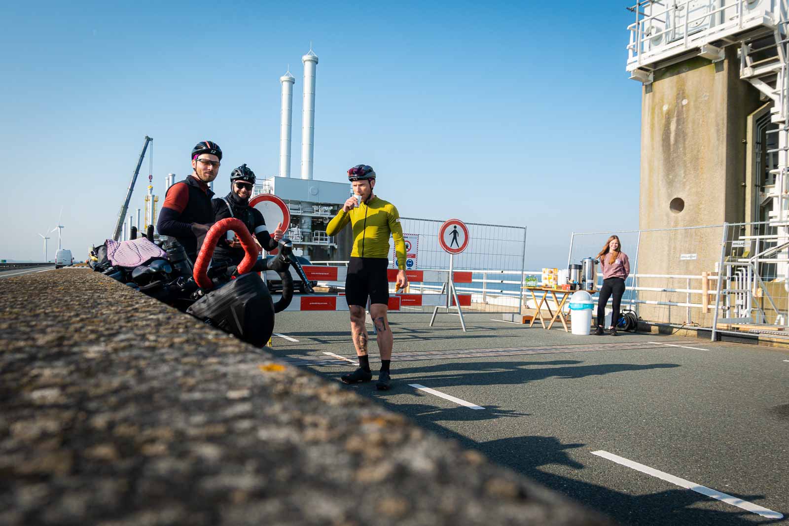 I ciclisti aspettano in un cantiere stradale e bevono un caffè Tre ciclisti aspettano in un cantiere per la costruzione di un ponte, bevendo caffè e mangiando biscotti