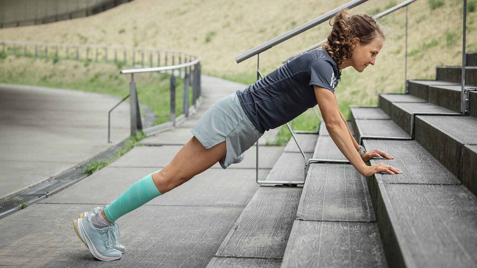 I push-up vanno persino all'aperto La donna fa push-up su un pavimento di cemento sullo sfondo che un uomo si estende su un muro