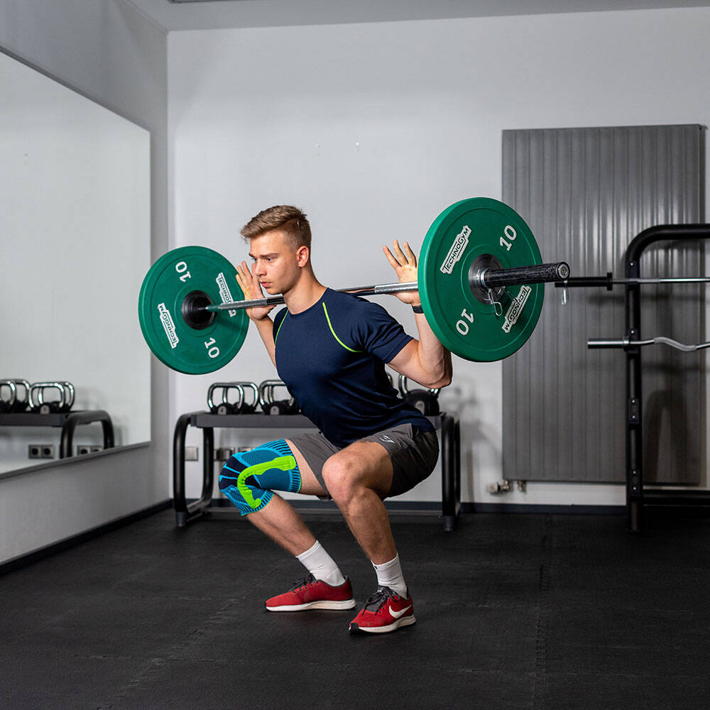 L'uomo in palestra con un tandage al ginocchio fa uno squat con un bilanciere sul retro