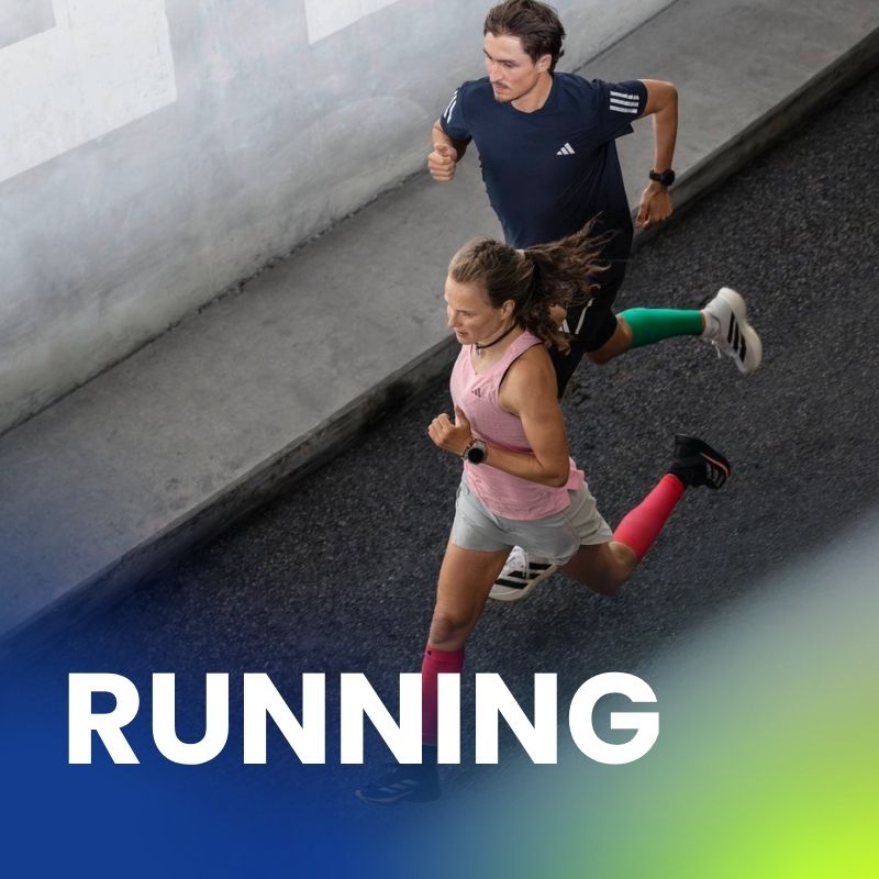 Una donna e un uomo corrono fianco a fianco su una strada asfaltata, indossando abbigliamento sportivo e calze a compressione colorate. Lo scatto è dall’alto.