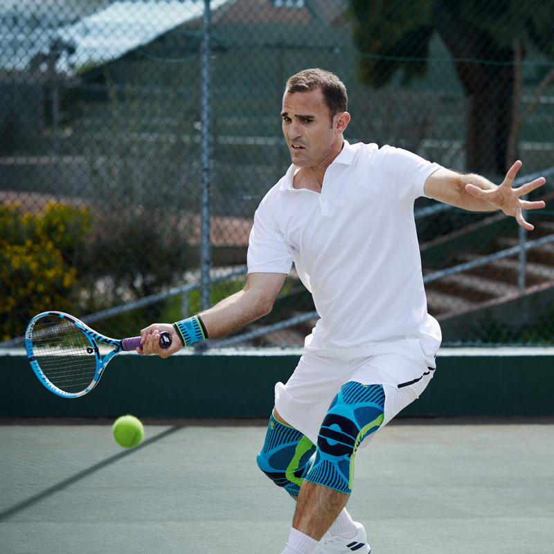 Tennis Player con abbigliamento da tennis bianco e barre del ginocchio sul colpo di diritto su un duro campo