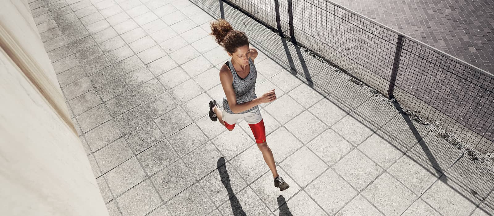 La donna corre su una superficie pavimentata urbana e indossa le maniche rosse della coscia