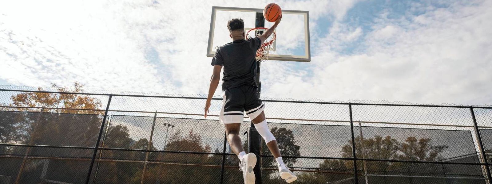 Il giocatore di basket salta su uno spazio libero al cestino e indossa una fascia bianca del ginocchio