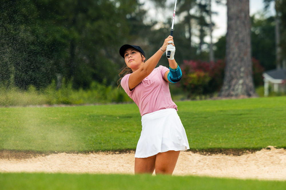 Golfista gioca dal bunker con una gomitiera per supporto e stabilità durante lo swing.