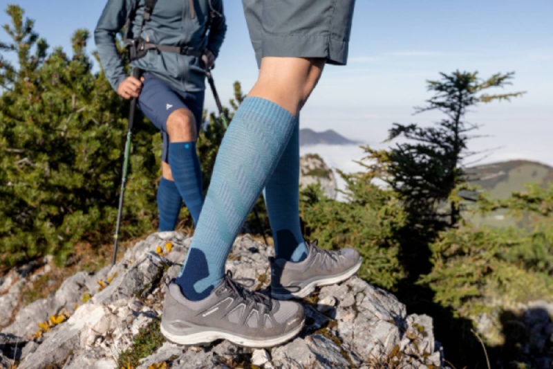 Due escursionisti con Outdoor Merino Compression Socks su un sentiero roccioso. Questi calzini a compressione offrono comfort ottimale e supporto per lunghe escursioni in un ambiente naturale.