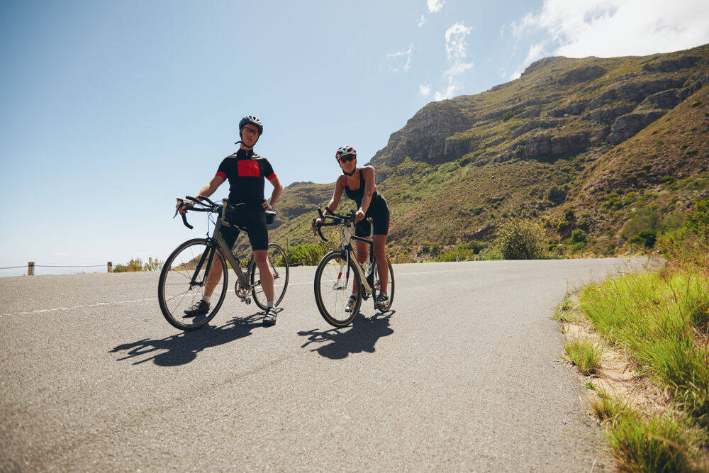 Un uomo e una donna con le sue bici da corsa si trovano su una strada in montagna