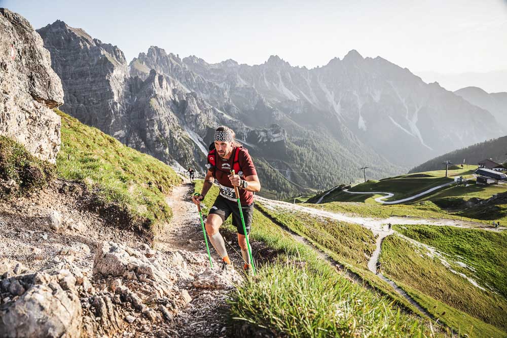 Ultrarunner durante una ripida salita con bastoncini su un trail alpino