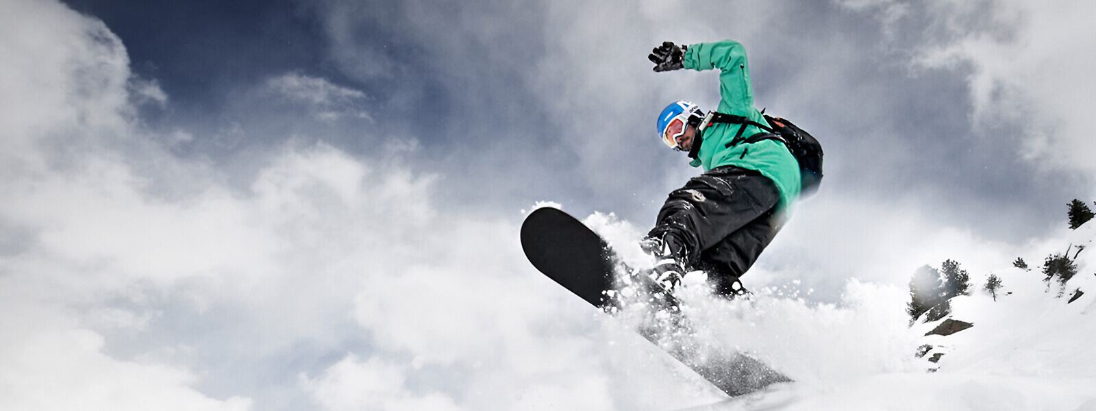 Prospettiva della rana: gli snowboarder in una giacca verde provengono dall'alto sopra una tavola crestata e si può vedere molta neve sussurrata