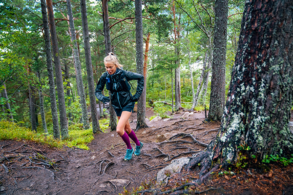 Traill Runner con calzini a lunga durata e giacca da allenamento corrono un percorso forestale con molte radici