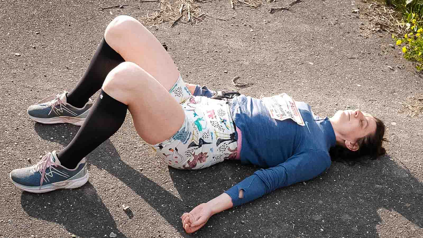 Rilassatevi dopo la corsa del Rennsteig con le calze da recupero Bauerfeind Una donna con calzini al ginocchio giace esausta a terra con le gambe piegate dopo la corsa di Rennsteig