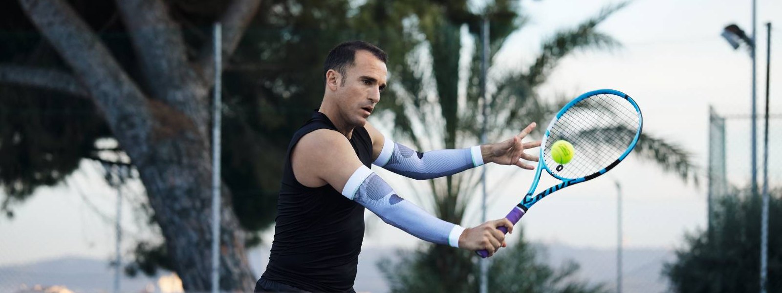 Maniche a braccio: il tuo compagno perfetto nel tennis Tennis Player con maniche a braccio bianco gioca a tennis e batte una palla con il rovescio