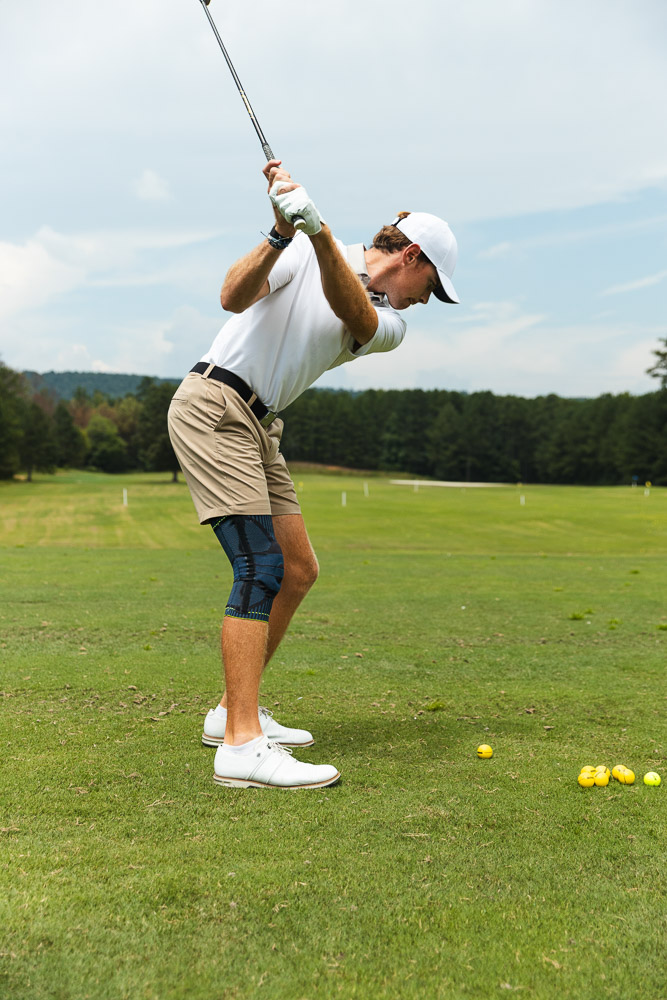 Golfista esegue uno swing sul campo con ginocchiera per stabilità e supporto durante il golf.