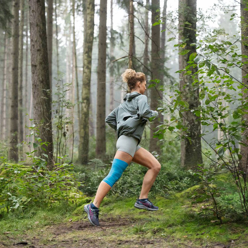 Una corridrice con una fasciatura al ginocchio corre attraverso un fitto bosco