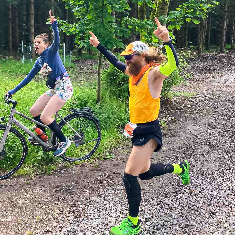Tifare fino al traguardo in bicicletta e a piedi Un uomo corre esultante verso il traguardo mentre una donna lo affianca in bicicletta.