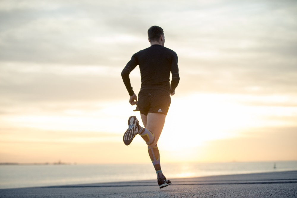 L'uomo con calze a lungo correre corre su un lungomare verso il tramonto