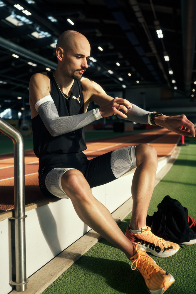 Il maratoneta Hendrik Pfeiffer è seduto a bordo pista indoor e indossa maniche compressive come parte della preparazione alla gara.