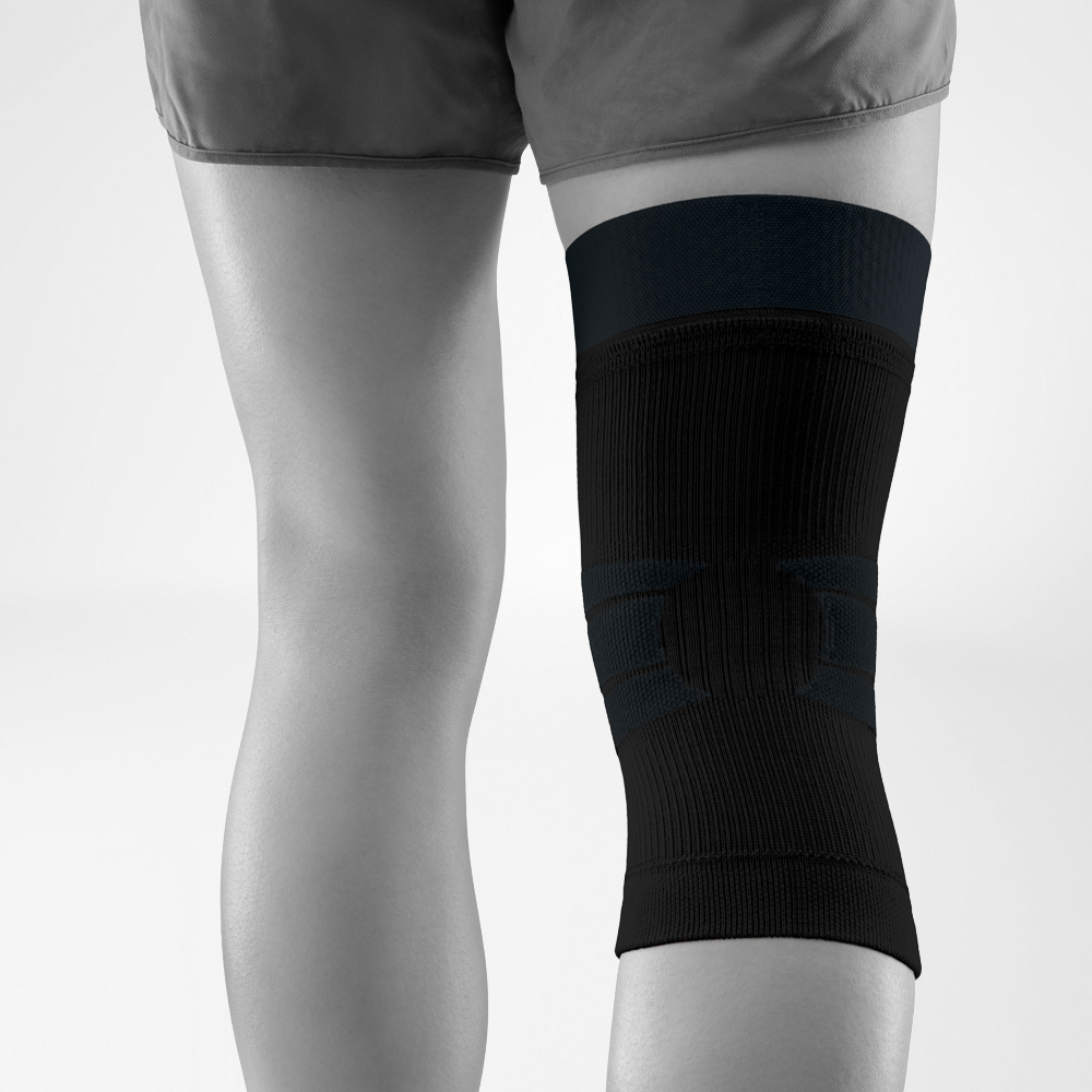 Vista posteriore di una ginocchiera nera indossata. Il design anatomico in tessuto a maglia con stabilizzazione integrata avvolge il ginocchio in sicurezza e lascia libertà di movimento.