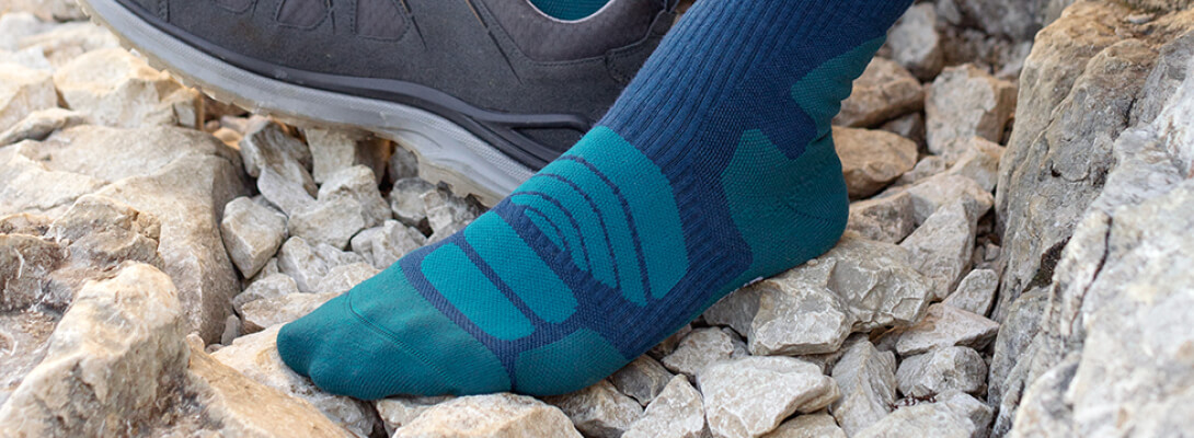 Calzini da trekking di mezza lunghezza blu scuro durante una pausa escursionistica Vista dettagliata di un piede con merino medio -lungo - calzini escursionistici su una superficie pietrosa - senza scarpe