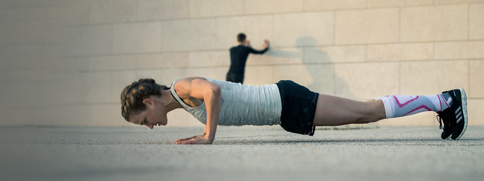 La donna fa push-up su un pavimento di cemento sullo sfondo che un uomo si estende su un muro
