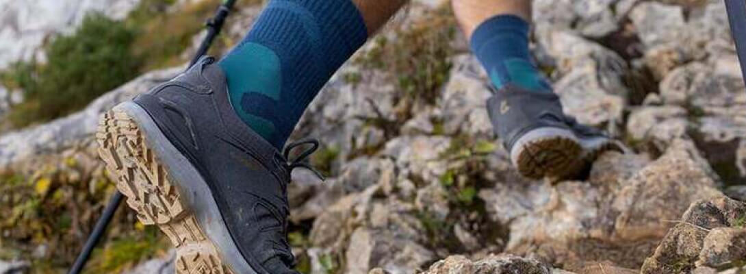 Persona che cammina sulle pietre di una montagna indossando calze da trekking di media lunghezza
