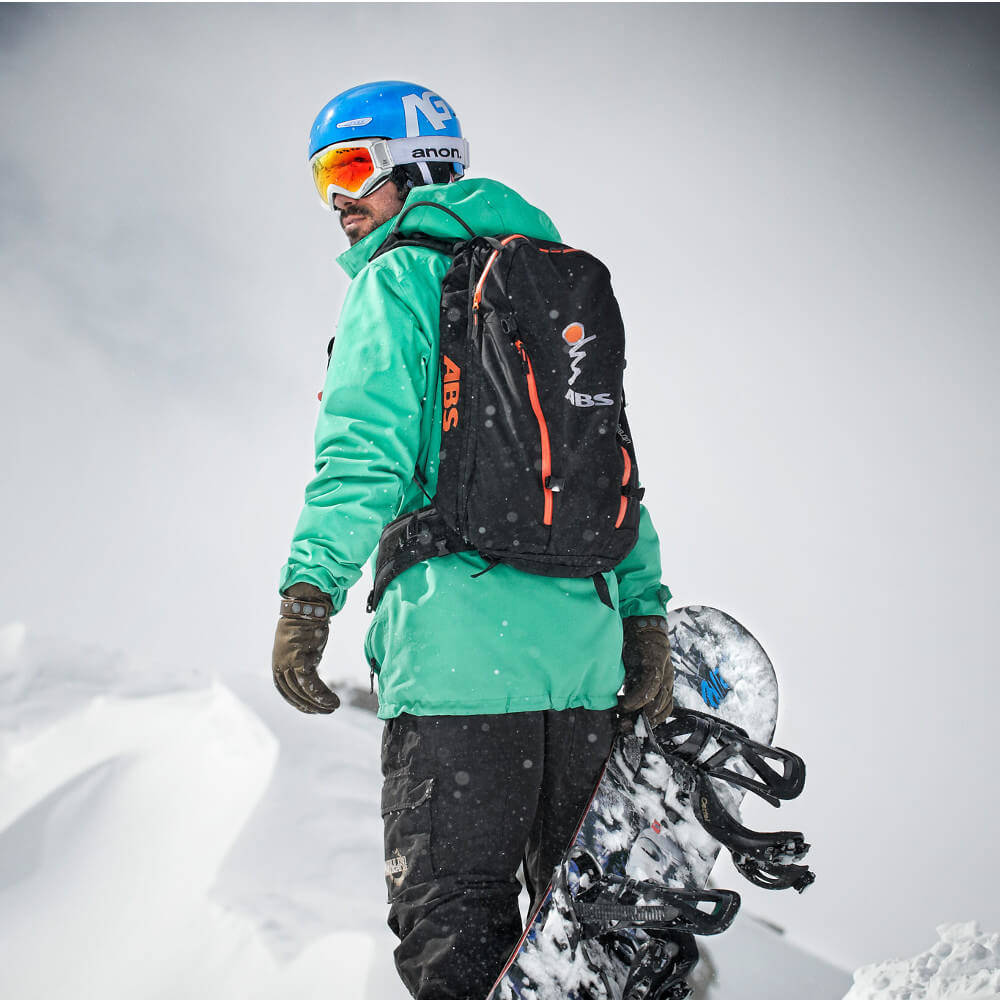 Quali cosce potenti fanno lo snowboard? Come posso rafforzare la mia schiena? Abbiamo alcuni suggerimenti Snowboarder con una giacca verde e una tavola in mano si guardano sopra la spalla all'indietro