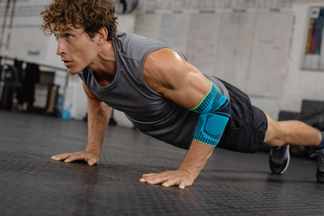 Giovane con la benda del gomito fa push-up sul pavimento di una sala di allenamento