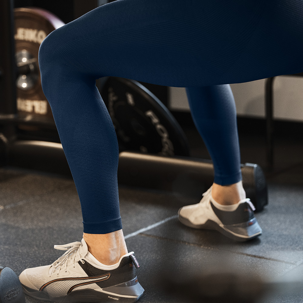 Stabilità dalle fondamenta – Tights compressivi per l’allenamento delle gambe Dettaglio delle gambe di un atleta con tights compressivi blu durante l’allenamento in palestra. Il tessuto aderente favorisce stabilità e circolazione.