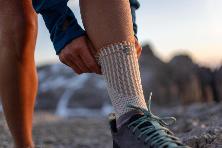 Un escursionista aggiusta la sua bandage da outdoor specializzata con polsino rinforzato. Sullo sfondo si vedono montagne e un tramonto.